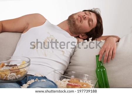 A lounger sleeping in a dirty clothes on a couch with snacks and beer
