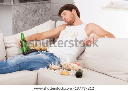 A wasted man in a dirty top with snacks and beer bottles