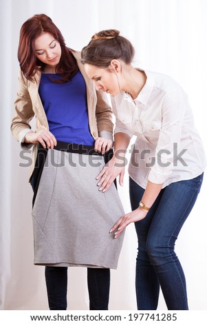 Two female friends trying on pencil skirt, vertical