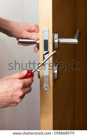 Hands repairing a door lock with a screwdriver