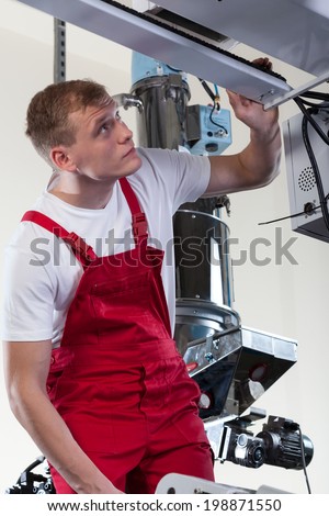Professional young mechanic repairing factory machine, vertical