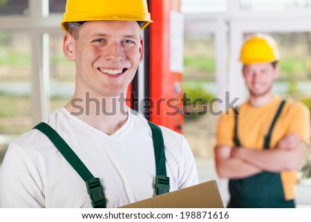 Portrait of a smiling factory worker and his collaborator in the background
