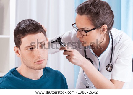 Young doctor examining patient\'s ears in his office