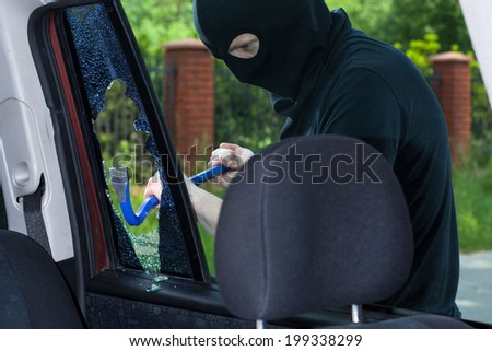 A burglar breaks a window with a crowbar in the car