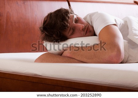 Young depressed man lying in bed and thinking about problems