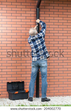 Back view of a man fixing gutters, vertical