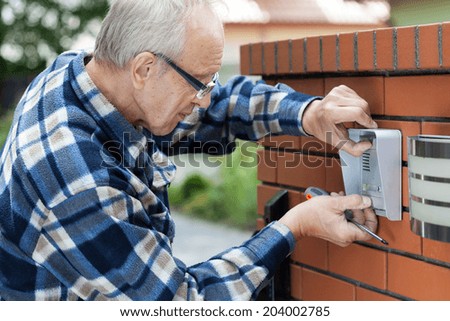 Handyman in flannel shirt fixing intercom, horizontal