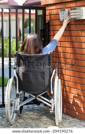 Independent woman on wheelchair dialing intercom, vertical