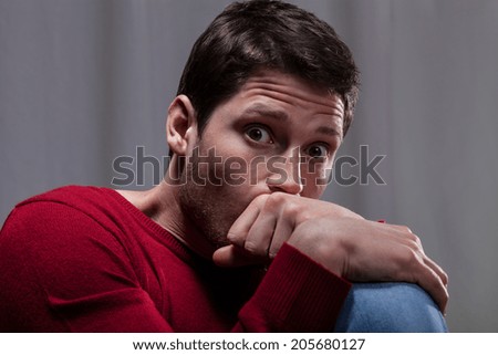 Young man with mental disease sitting curled up and scared