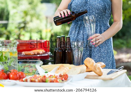 Woman pouring beer and preparing meals on barbecue