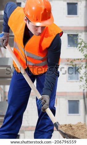 Construction worker digging sand with shovel, vertical
