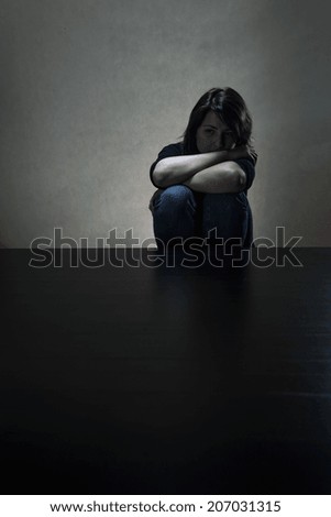 Sad girl sitting alone in dark room, vertical
