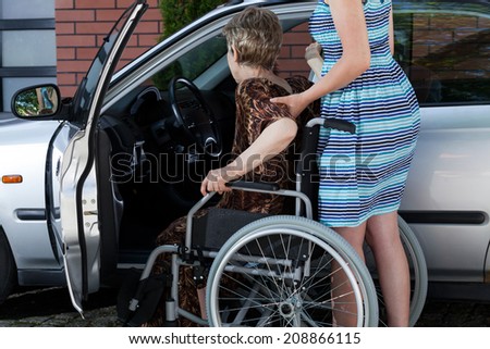 Young woman helping a disabled lady get in the car
