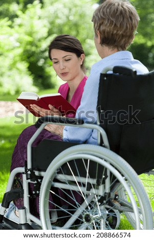 Nurse is reading a book with older woman in the park