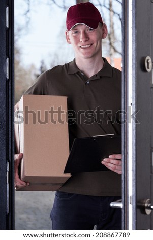 Young courier with order standing in door and waiting for pay