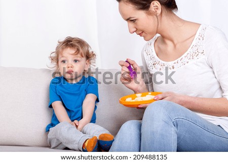 Young woman feeding her fussy child while sitting on a sofa