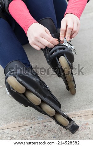 Teenage girl sitting on the ground and putting on her inline skates
