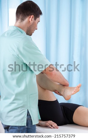 Physiotherapist bending knee of patient lying on treatment couch