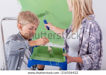 Cute little son helping his mother painting a wall