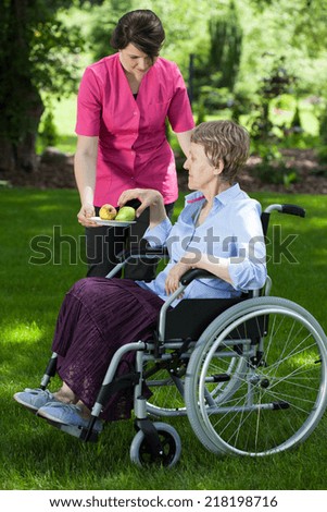 Caregiver giving fresh and healthy pear to disabled senior woman