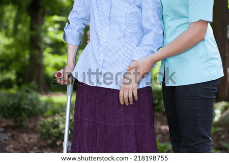 Close-up of nurse walking together with a female patient with a crutch