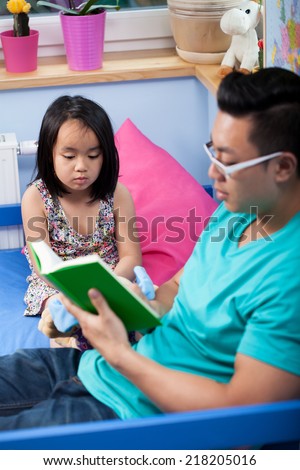 Asian dad reading a fairytale to daughter