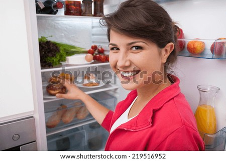 Smiling young woman taking doughnut from fridge