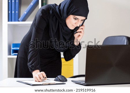 Arab office worker using laptop and talking on the phone