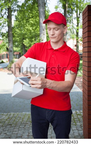 Delivery man carrying a box and looking at tablet