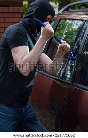 Masked robber breaks car window with a crowbar