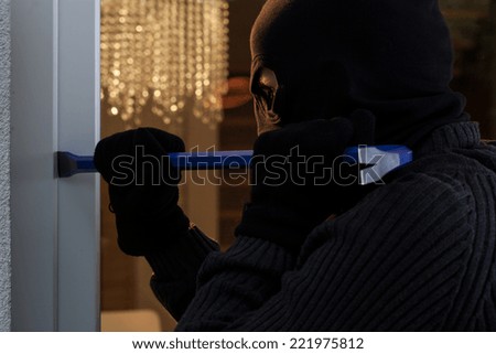 Dangerous burglar open the window with a crowbar