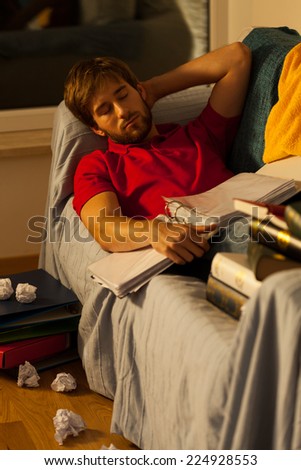 Young student sleeping surrounded by books and papers