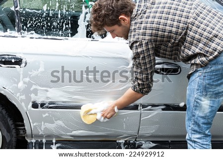 Young handsome guy cleaning his silver auto