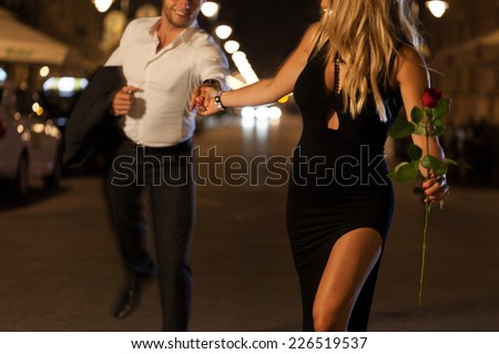 An elegant couple holding hands when running on a date at night