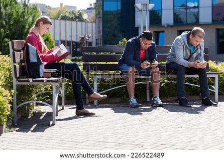 Boys using phones and girl learning outside