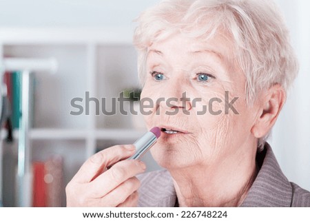 Senior woman looking at mirror and applying lipstick
