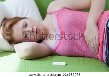 Teenager lying on bed with positive result of pregnancy test