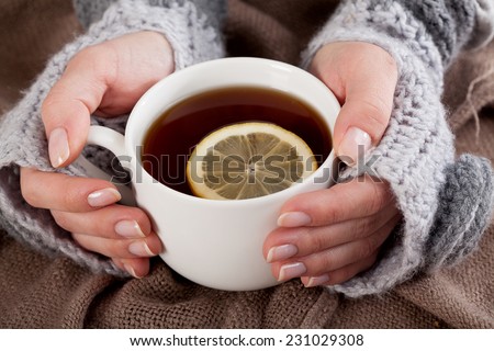 Woman\'s hand holding cup of tea with lemon on a cold day