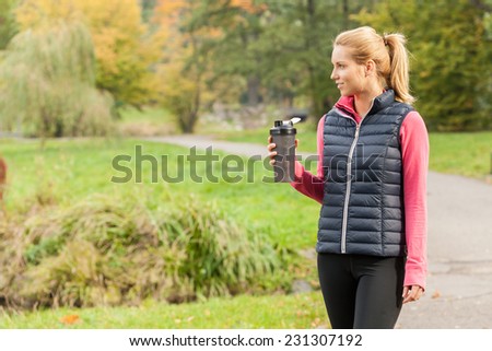 Photo of young woman drinking from water bottle after jogging