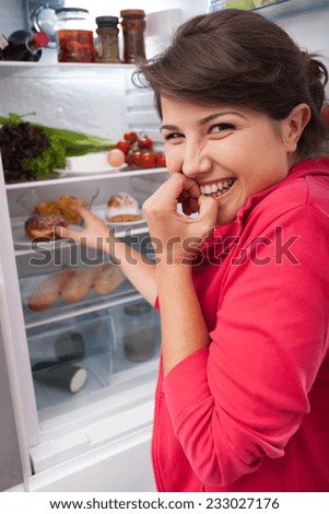 Young greedy girl reaching for the delicious donut in the fridge