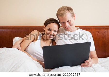 A happy man and woman hugging in bed with their laptop