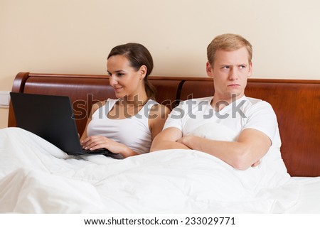 A woman on her laptop and an angry bored man in bed