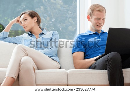 A bored woman and a happy man playing on a couch