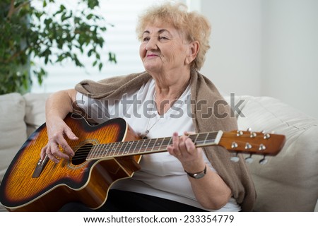 Aged happy woman playing the guitar in her room