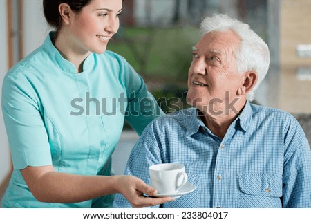 Helper giving senior man cup of coffee