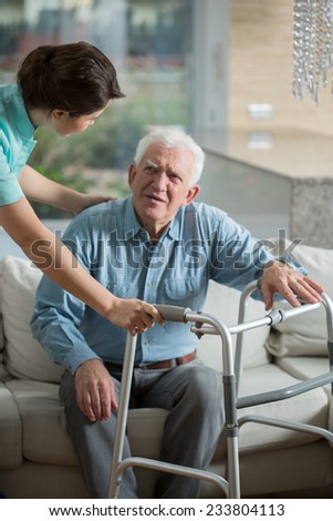 Disabled man using walking frame and helpful nurse