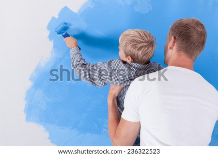Horizontal view of boy painting wall in dad\'s arms