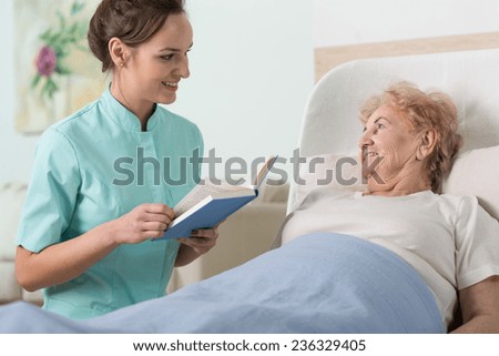 Young beautiful nurse reading to sick older woman in bed