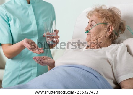 Young nurse giving the pills to sick aged woman