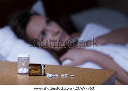 Sleeping pills lying on night table and woman trying to sleep